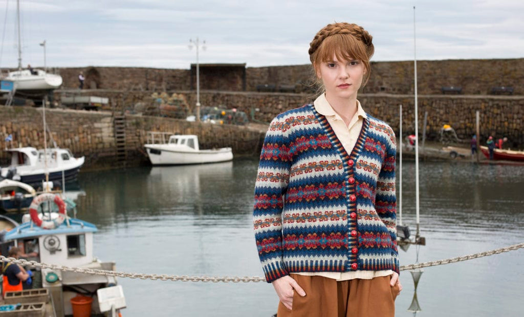 Woman wearing a patterned cardigan standing by a harbor with boats.