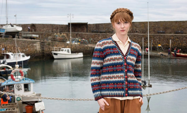 Woman wearing a patterned cardigan standing by a harbor with boats.