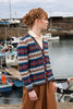 Woman wearing a patterned cardigan by a harbor with boats in the background