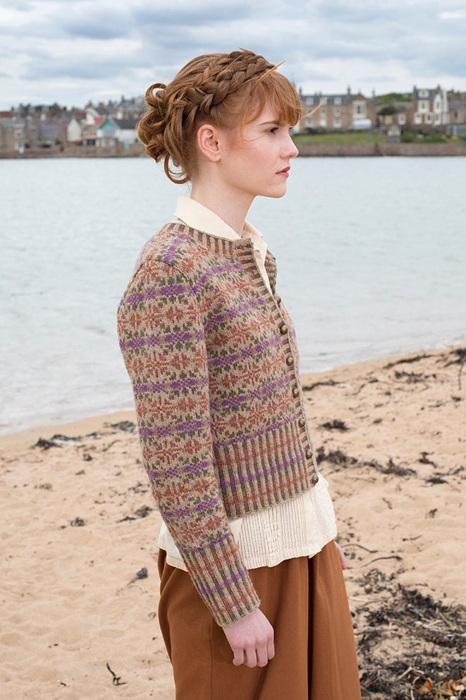 Woman wearing a patterned sweater on a beach with water and houses in the background