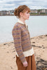 Woman wearing a patterned sweater on a beach with water and houses in the background