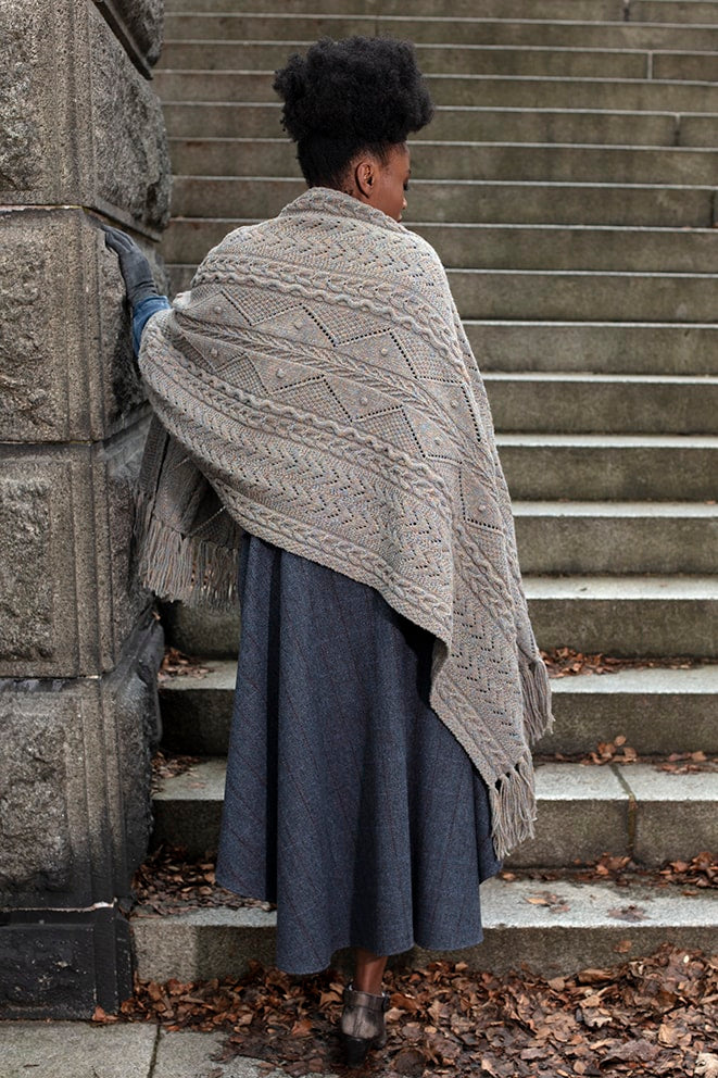Person wrapped in a patterned shawl standing on stone steps.