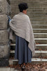Person wrapped in a patterned shawl standing on stone steps.