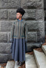 Woman wearing a patterned coat and long skirt standing against a stone wall.
