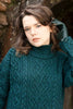 Woman wearing a teal knitted sweater with a stone wall background