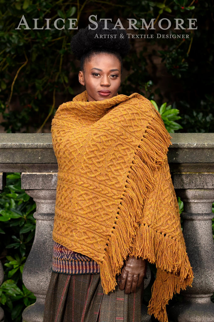 Woman wearing a mustard yellow textured shawl with fringes, standing outdoors.