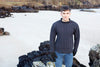 Man wearing a dark sweater and jeans standing on a rocky beach.