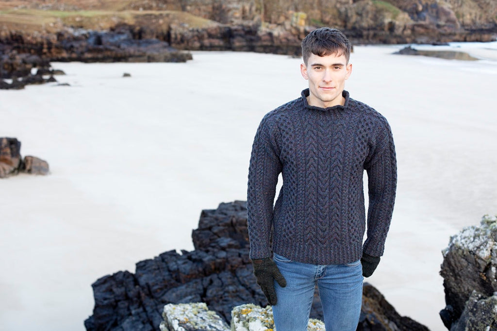 Man wearing a dark sweater and jeans standing on a rocky beach.