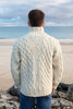 Man wearing a cream cable knit sweater standing on a beach with ocean view