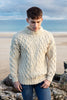 Man wearing a patterned sweater standing on a beach with rocks and water in the background