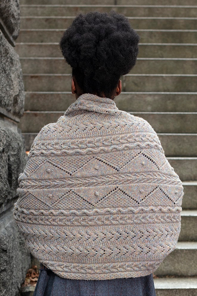 Person wearing a patterned knitted sweater standing on stone steps.