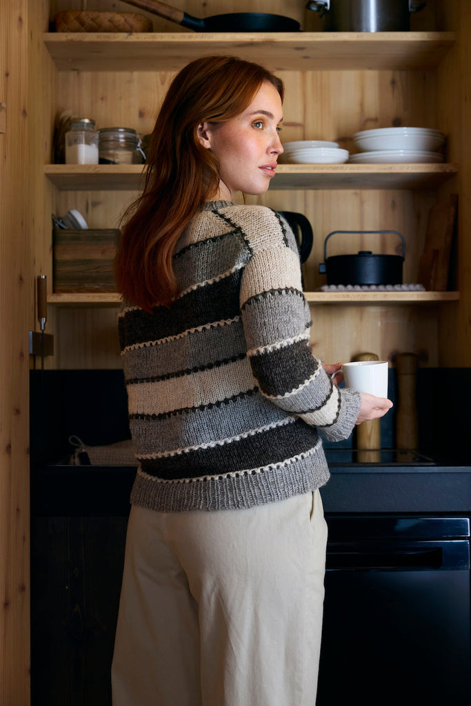 Woman in a striped sweater holding a mug in a kitchen.