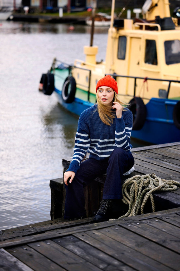 Woman sitting on a dock by a body of water with a boat in the background