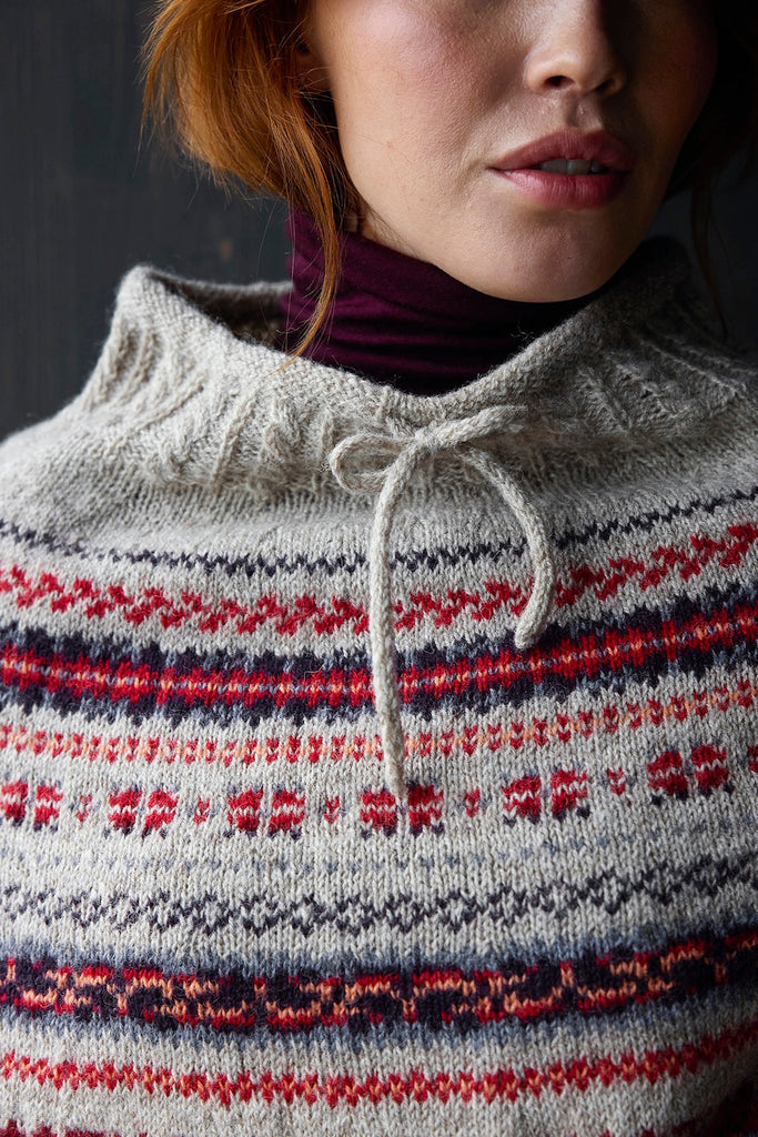 Person wearing a knitted sweater with a pattern of red, blue, and gray.