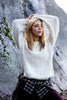 Woman wearing a white sweater and plaid shirt against a rocky background
