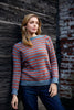 Woman wearing a blue and red striped sweater against a textured wall.