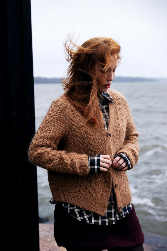 Person wearing a brown knitted cardigan by a body of water