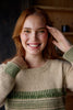 Woman wearing a beige sweater with green patterns, smiling indoors.