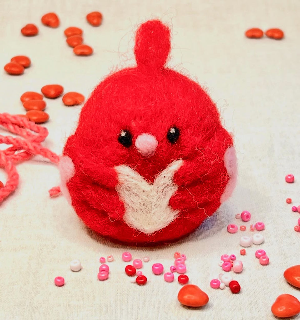 Red plush toy with a white heart surrounded by small red and pink objects on a light background