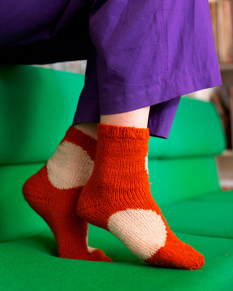 Person wearing orange socks with white hearts on a green couch