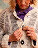 Person wearing a textured cardigan over a purple shirt, buttoning it up.