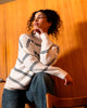 Woman wearing a white sweater with black stripes sitting against a wooden wall.