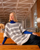 Woman sitting on a wooden bench wearing a striped sweater and blue turtleneck in a modern indoor setting.