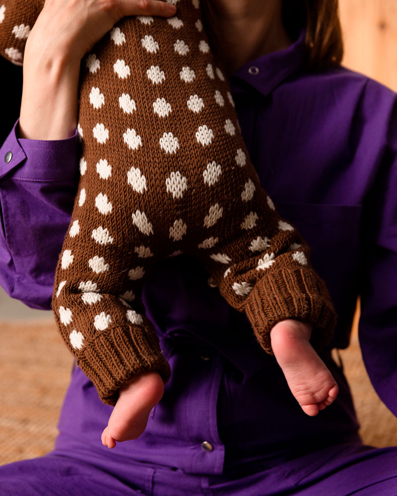 Person wearing a brown sweater with white polka dots, held by another person in a purple shirt.