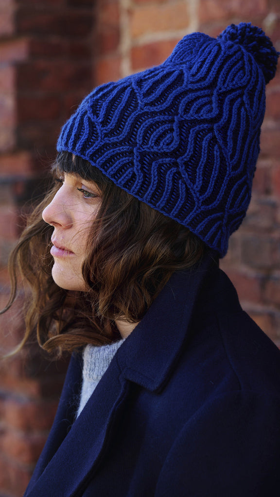 Person wearing a blue knitted beanie against a brick wall