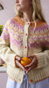 Person wearing a patterned cardigan holding an orange in a kitchen setting