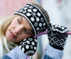 Person wearing a black and white patterned knitted hat and mittens, with a blurred background.