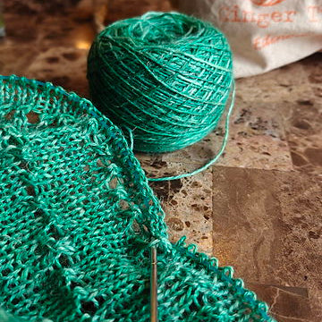 Green knitted fabric and yarn on a kitchen counter with a bag in the background