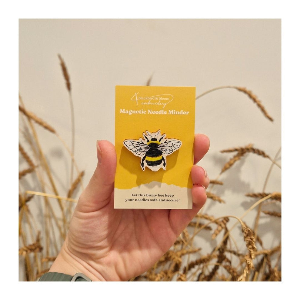 Hand holding a yellow card with a bee design against a natural background