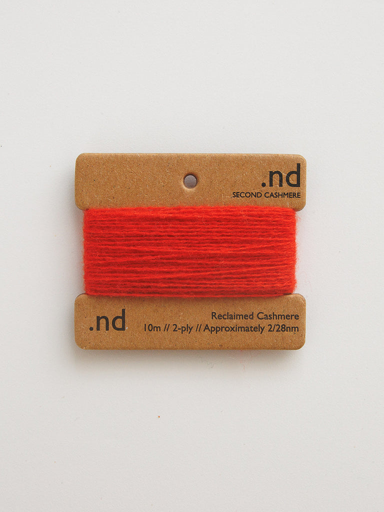 Red yarn on a cardboard holder with 'nd' branding on a light gray background