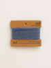 Blue yarn swatch on a cardboard card with 'nd' branding on a beige background