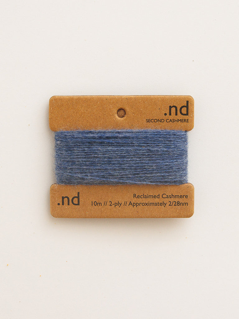 Blue yarn swatch on a cardboard card with 'nd' branding on a beige background