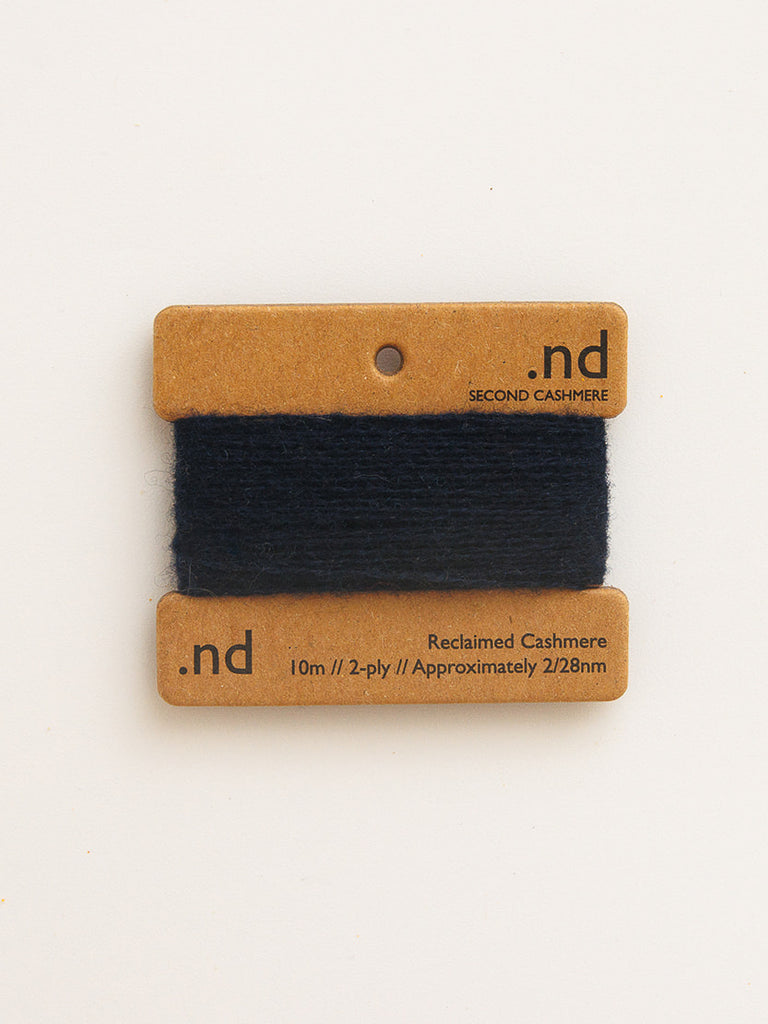 Black yarn on a branded brown card with 'nd' branding on a beige background