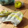 Knitted item with yellow accents on a wooden surface, accompanied by yarn balls.