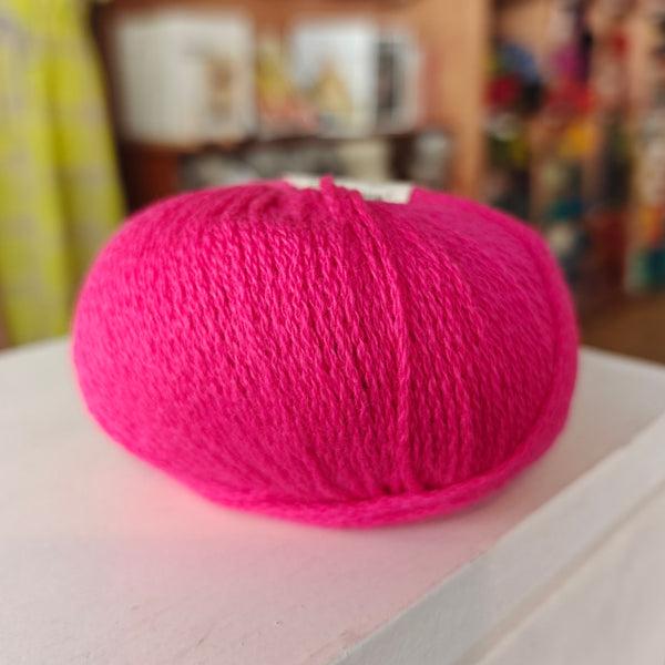 Three skeins of Gepard Cashmere Klassik yarn in orange, pink, and green colors, displayed on a surface.