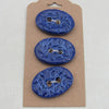 Three blue ceramic buttons on a cardboard backing with a white background