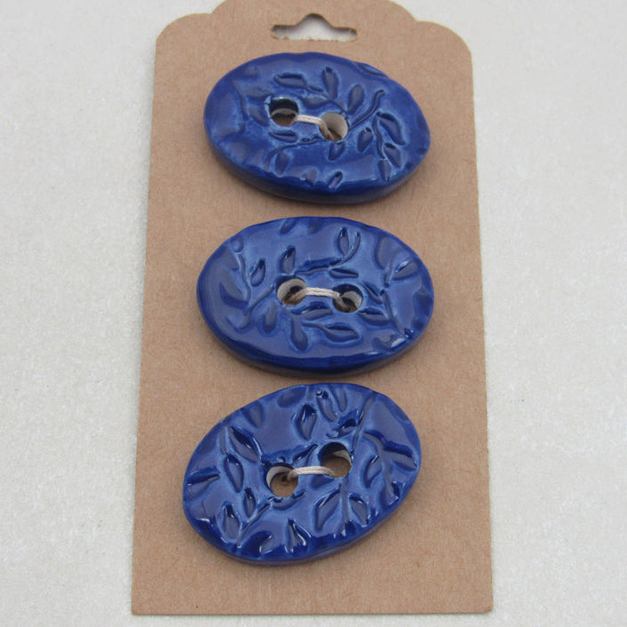Three blue ceramic buttons on a cardboard backing with a white background