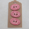 Three pink floral-patterned buttons on a cardboard backing against a light gray background