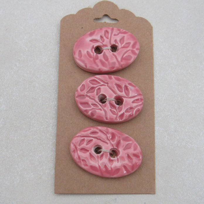 Three pink floral-patterned buttons on a cardboard backing against a light gray background