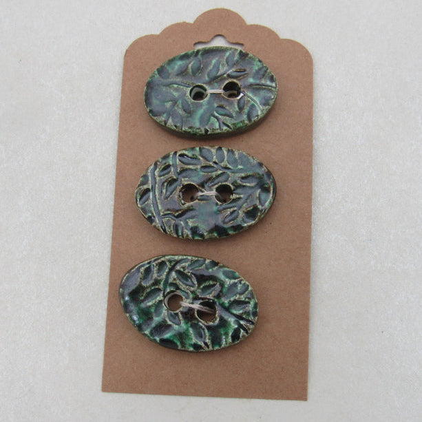 Three green ceramic buttons on a brown card against a white background