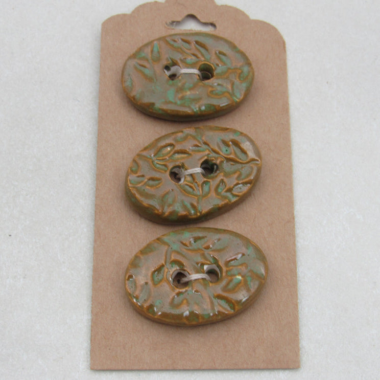 Three ceramic buttons with floral patterns on a cardboard backing against a white background