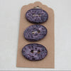 Three purple buttons on a cardboard backing against a white background