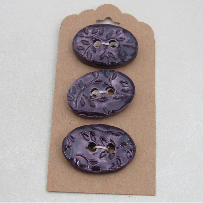Three purple buttons on a cardboard backing against a white background
