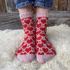 Red and white heart-patterned socks worn by a person on a fluffy white rug.