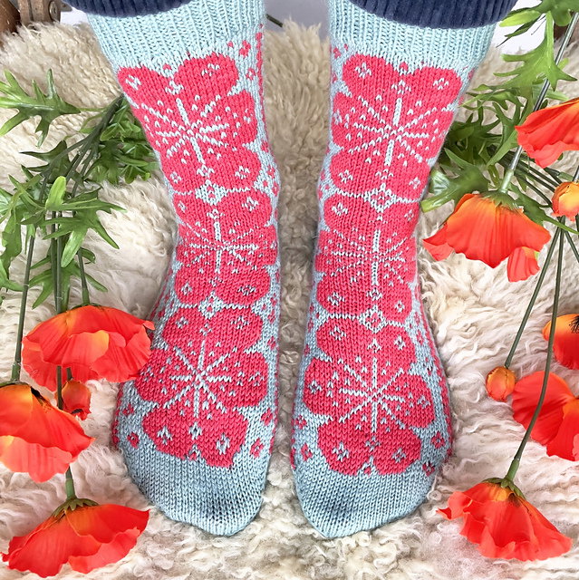 Pair of socks with pink floral pattern on a soft surface with flowers around