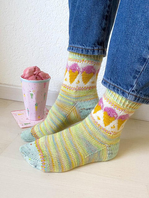Colorful knitted socks worn with blue jeans, next to a pink cup with ice cream.
